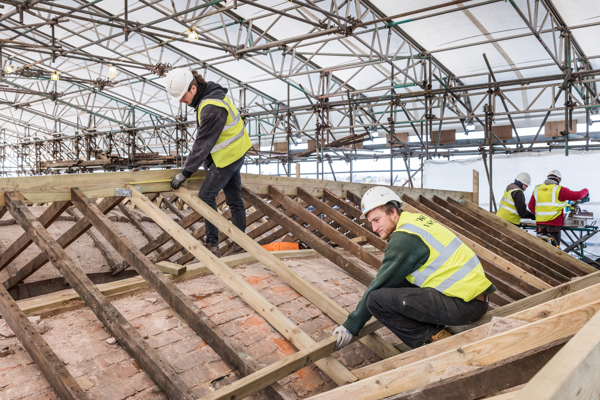 Two construction workers in high-vis jackets working on roof
