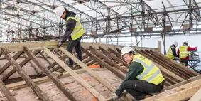 Two construction workers in high-vis jackets working on roof
