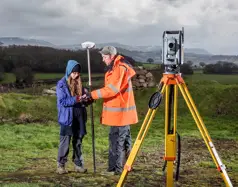 A man in a field teaching surveying techniques to a woman.
