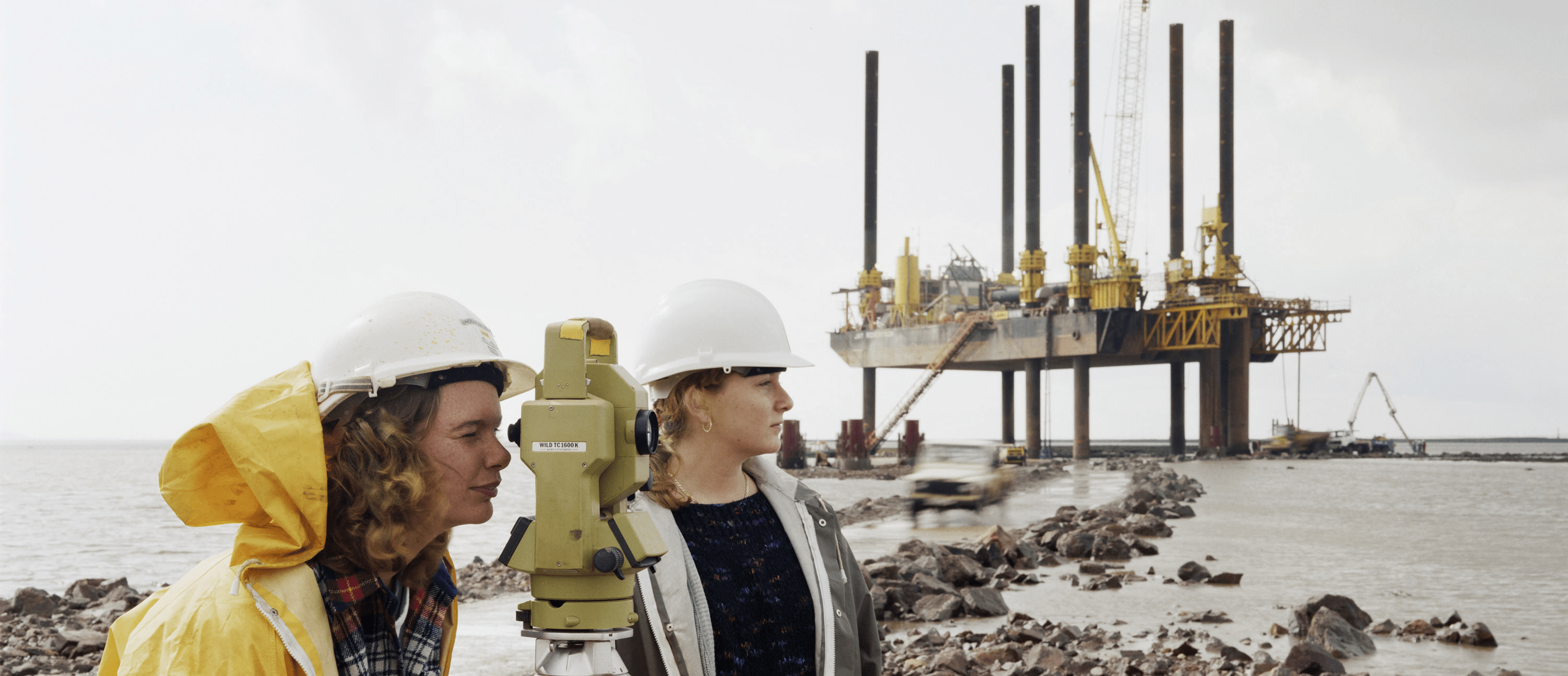 Two engineers using a theodolite at a construction site by the sea.