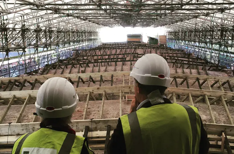 Two people overlooking repairs to an historic factory roof, surrounded by s